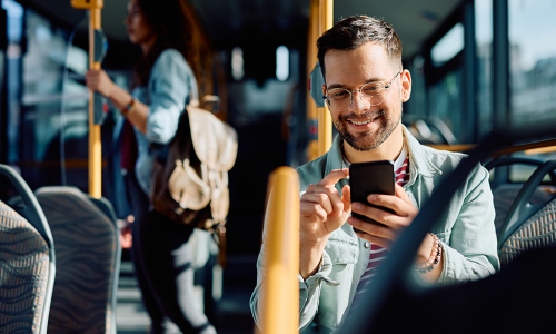 Junger Mann sitzt in einem Bus und bedient sein Smartphone.