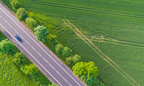 Ein Auto fährt auf einer Straße durch grüne Felder, Ansicht aus der Vogelperspektive (Bild: ©Christian Schwier - stock.adobe.com)