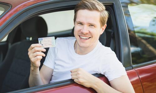 Junger Mann zeigt lachend seinen Führerschein