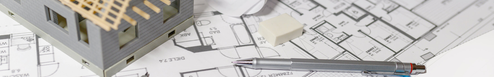 Grundrisszeichnung auf einem Tisch, darauf ein kleines Modellhaus, Lineal, Zirkel und Stift