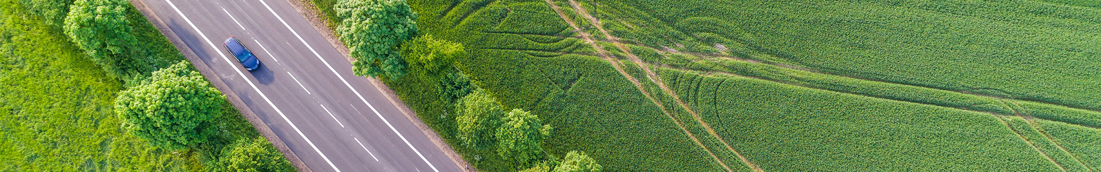 Ein Auto fährt auf einer Straße durch grüne Felder, Ansicht aus der Vogelperspektive (Bild: ©Christian Schwier - stock.adobe.com)