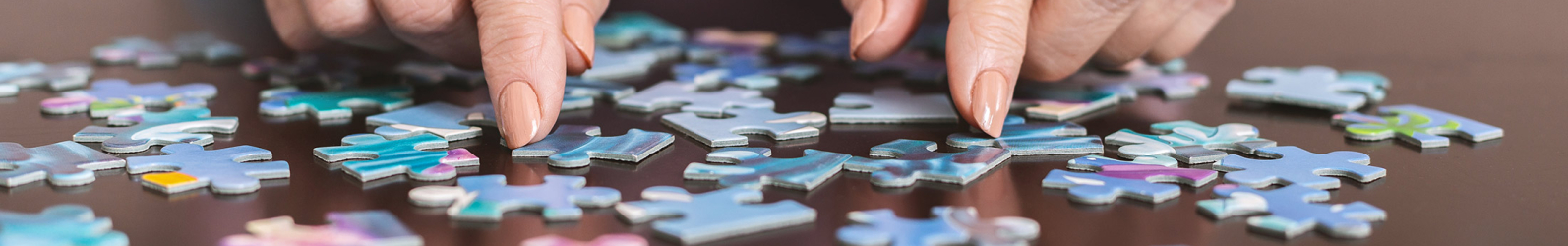 Ältere Damenhände sortieren Puzzleteile auf einem Tisch