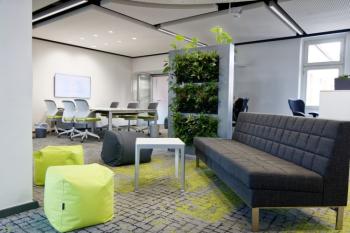 Sitzgruppe im Open-Space-Büro - graues Sofa, grüne Sitzsäcke, ein kleiner weißer Tisch