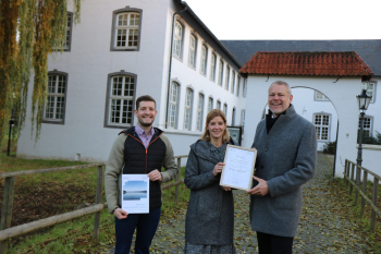 drei lächelnde Personen mit Bericht und Urkunde vor historischer Burg