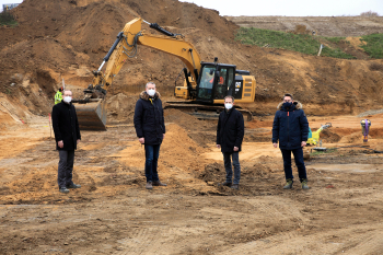 vier Personen auf Baustelle, dahinter Bagger und Sandberg