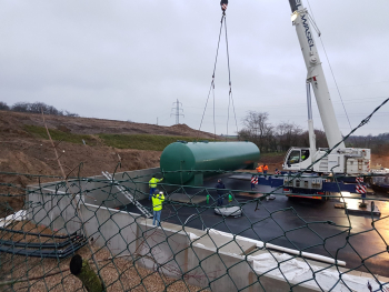 Kran stellt großen Behälter auf Baustelle ab.