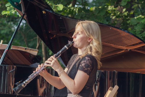 Musikerin spielt Klarinette, dahinter geöffneter Konzertflügel